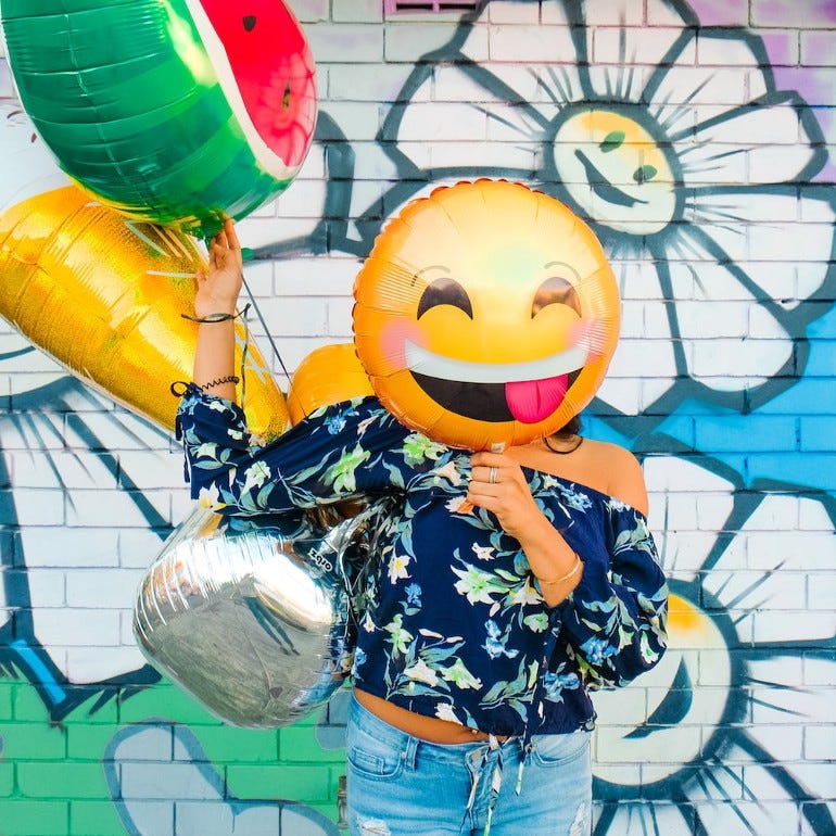 woman holding smiley face balloon over her face